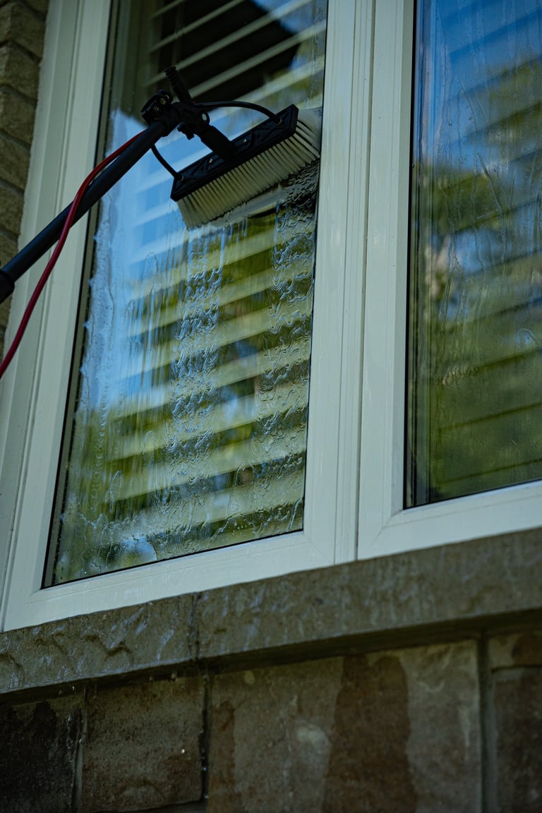 Cleaning window with soap brush attachment on pressure washer, revealing building reflection