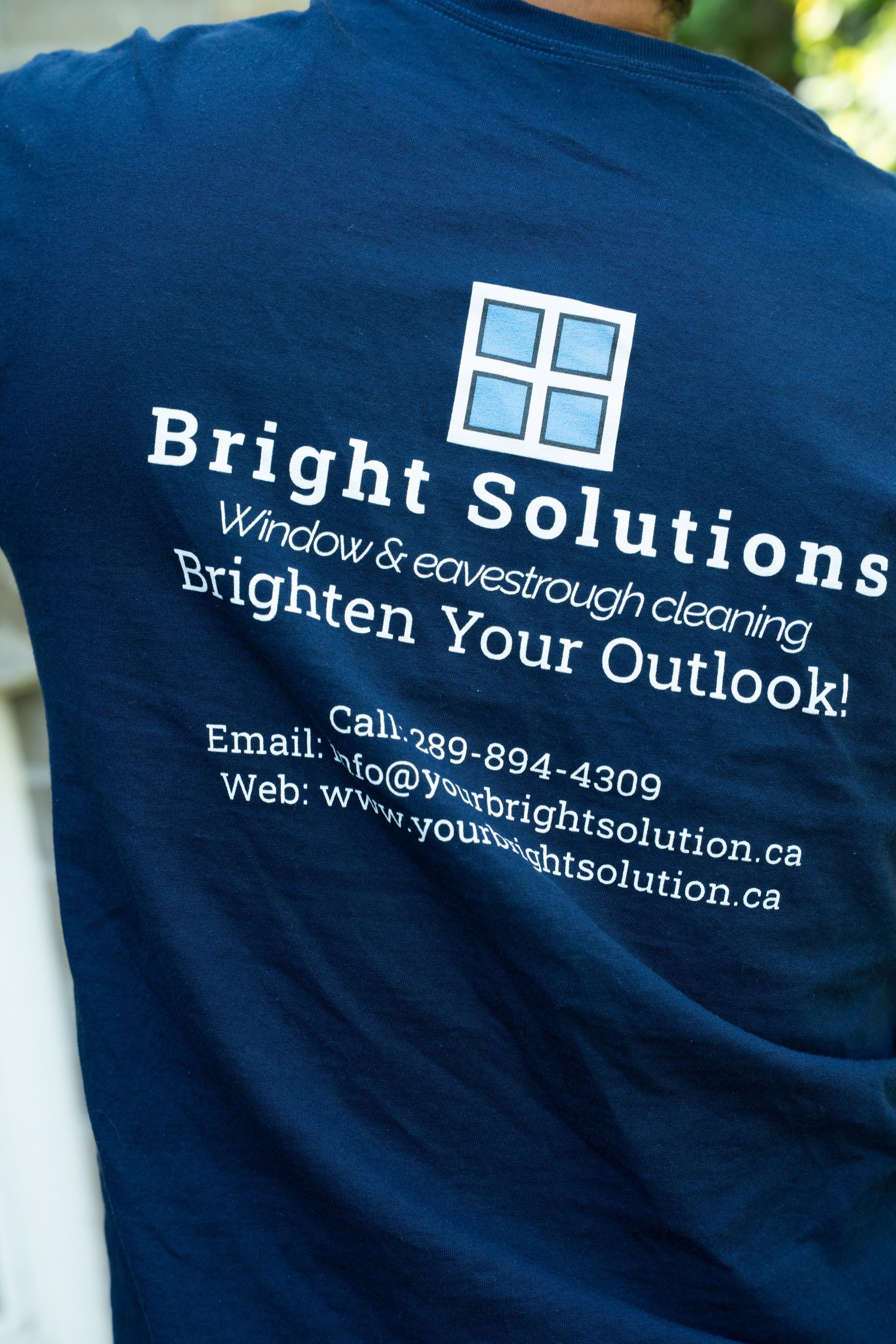 Navy blue t-shirt displaying Bright Solutions window cleaning business logo with contact information and tagline Brighten Your Outlook