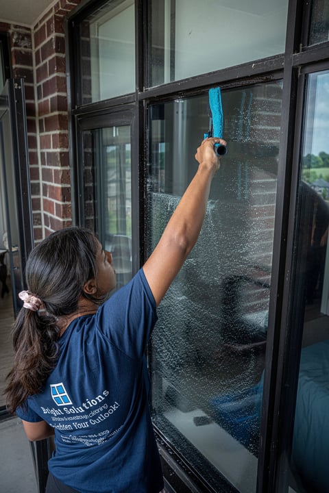 Worker cleaning glass windows with a blue squeegee, wearing a navy work shirt